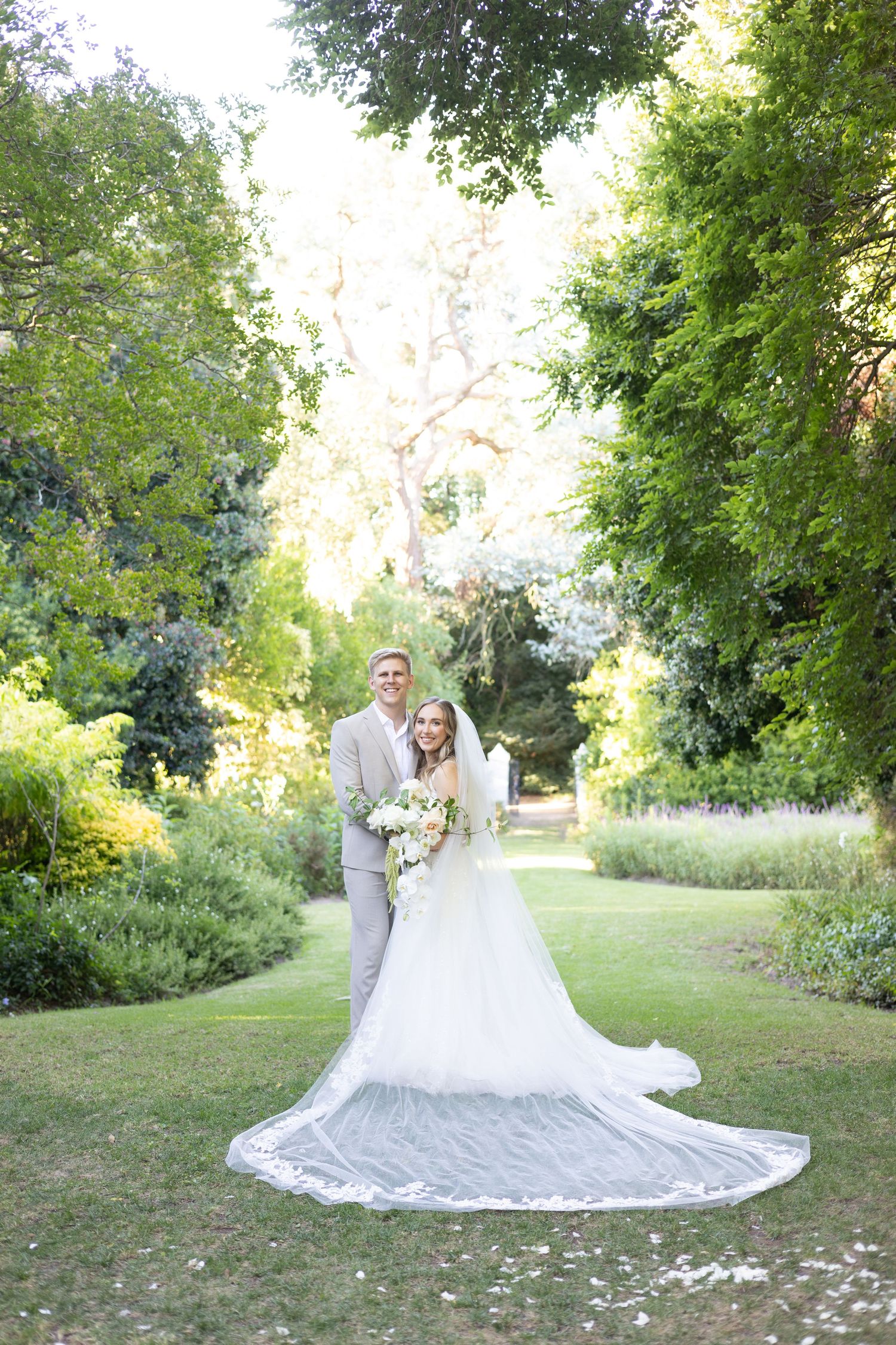 Elegant wedding portrait of a couple in a lush garden setting with a flowing cathedral veil.