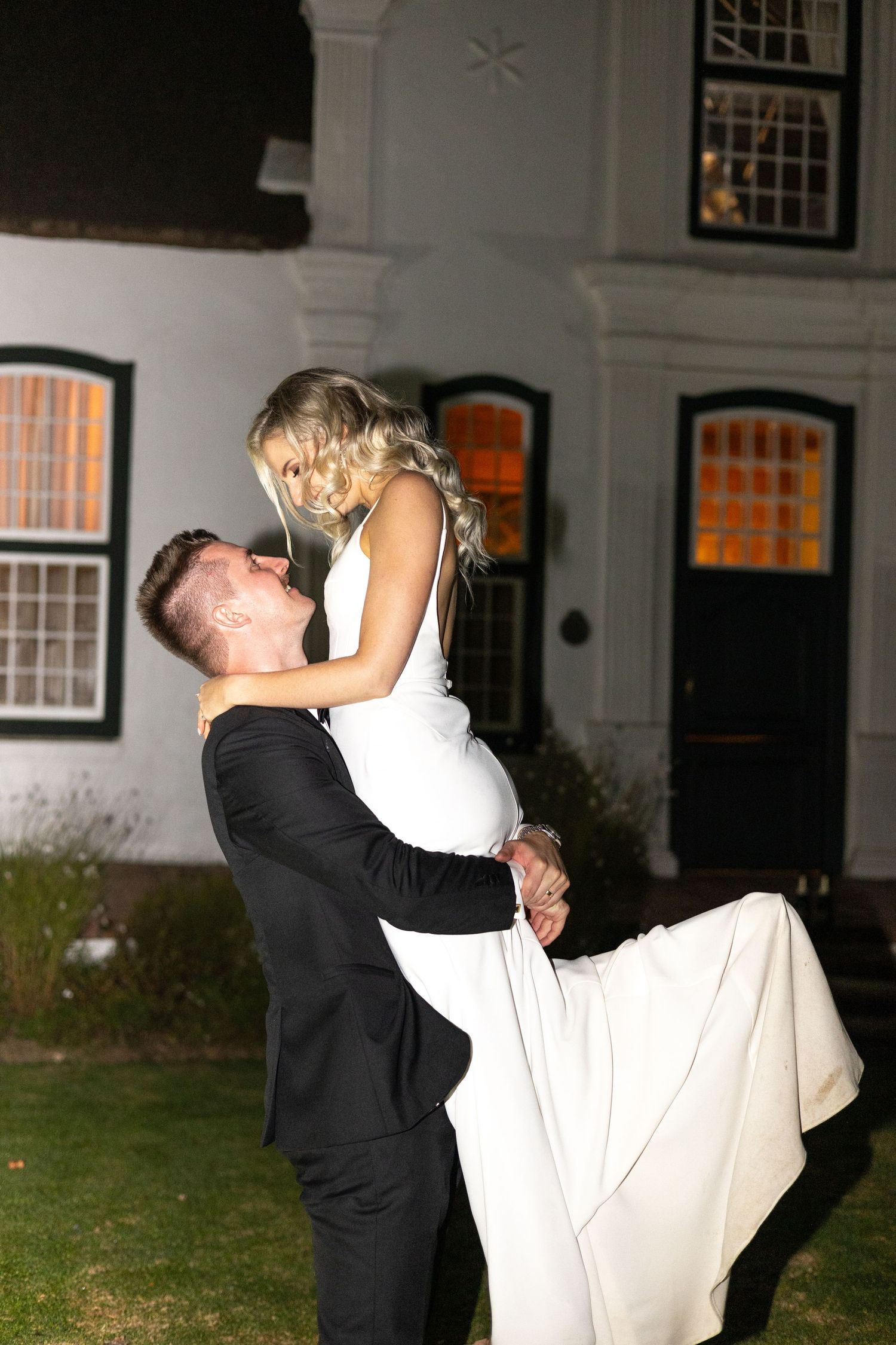 Playful nighttime wedding moment with couple in front of historic building.