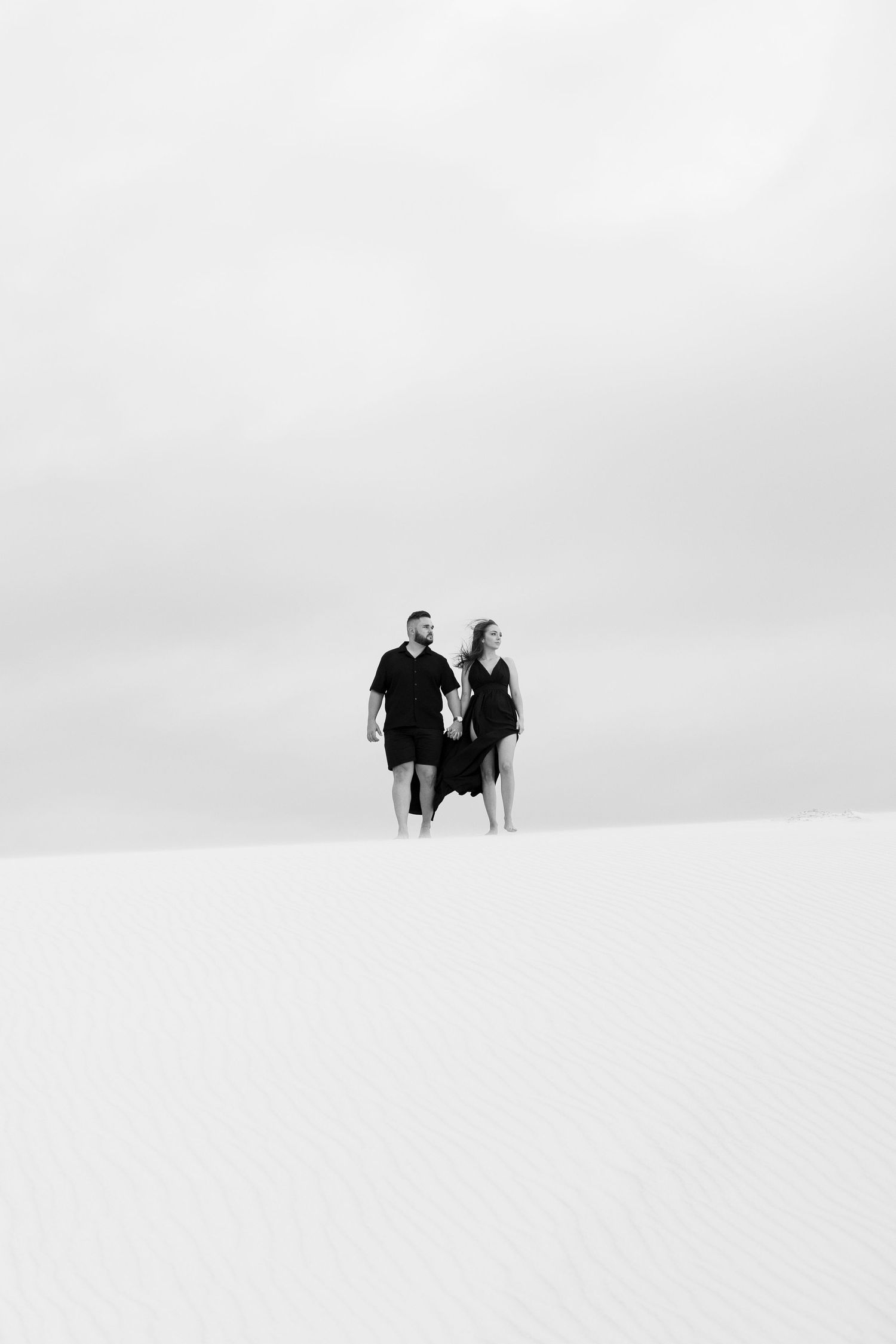 Two figures in black and white standing on a snowy hill against a minimalist backdrop.