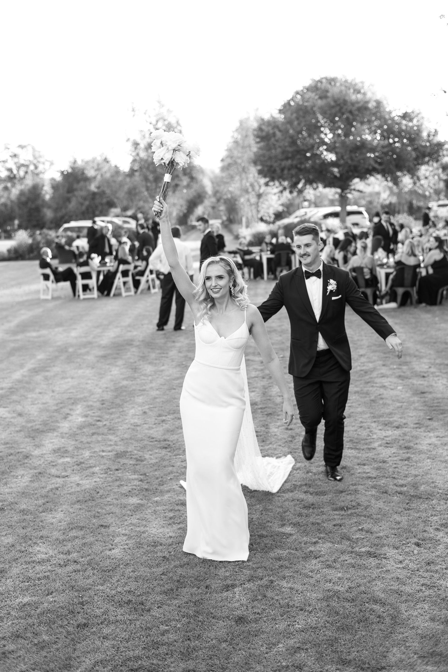 Black and white photo of newlyweds celebrating during outdoor garden reception.