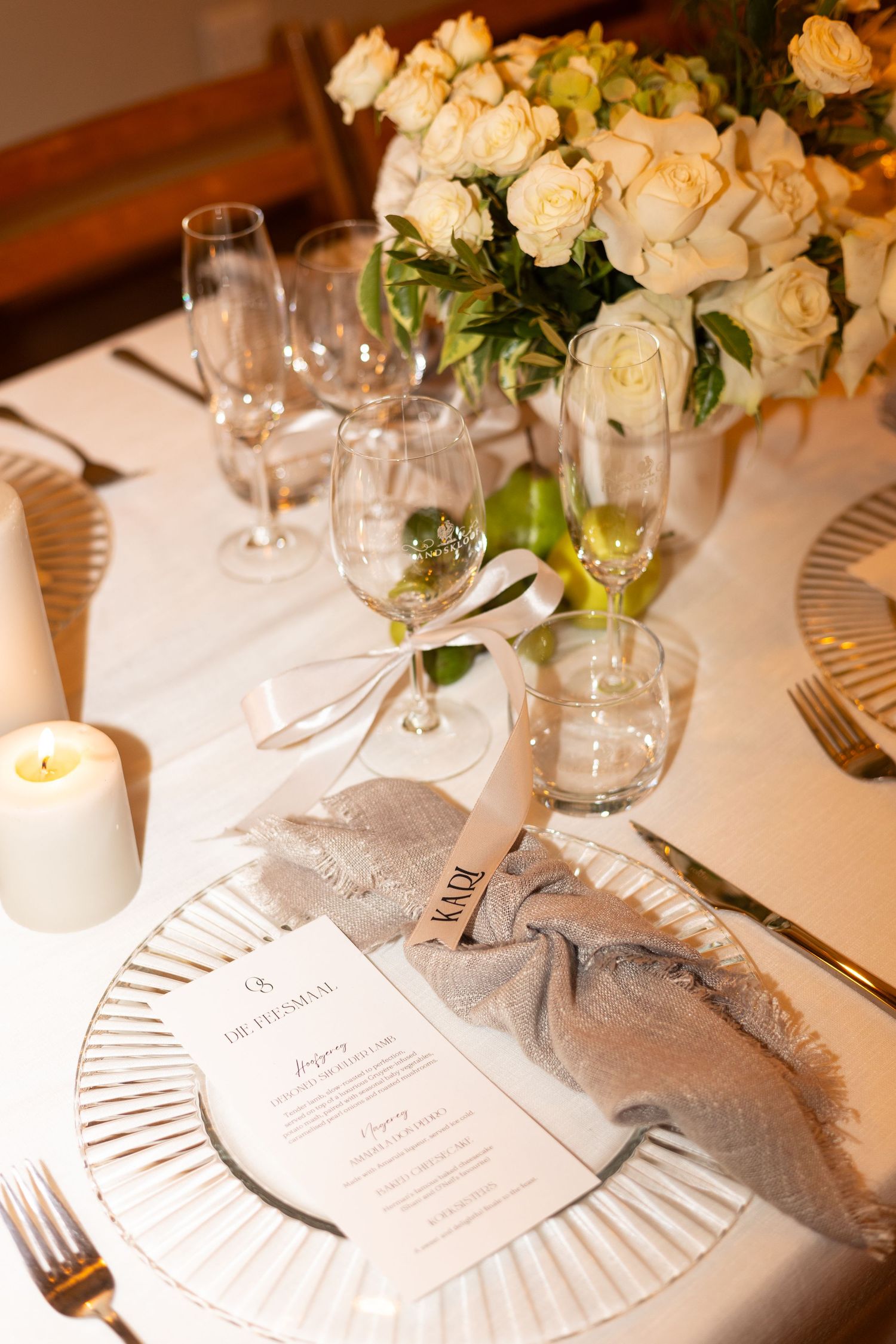 Elegant place setting at formal dinner with white roses, menu card, crystal glasses and white charger plate.