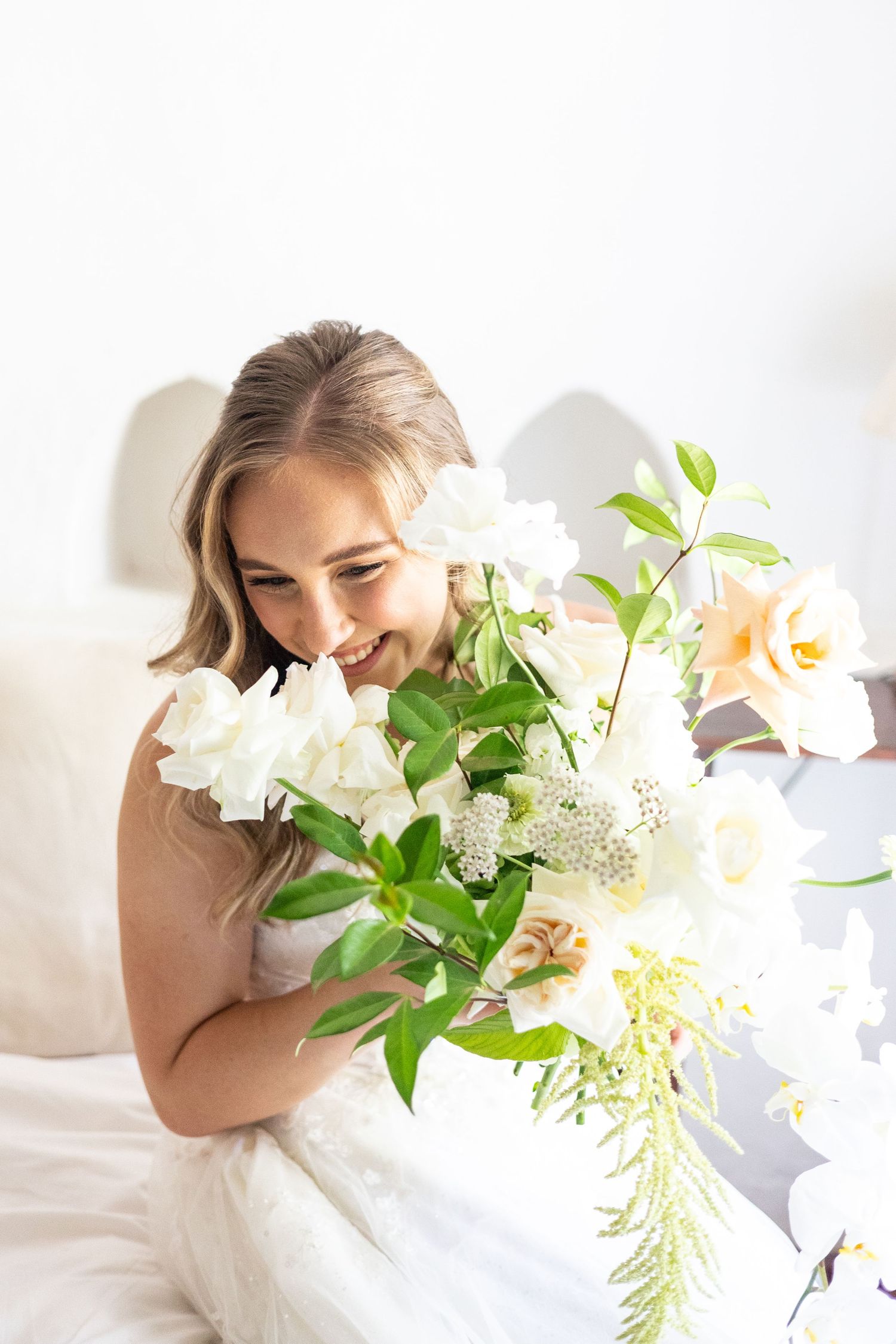 Soft and ethereal portrait featuring a white floral bouquet with lilies and greenery in bright natural light.