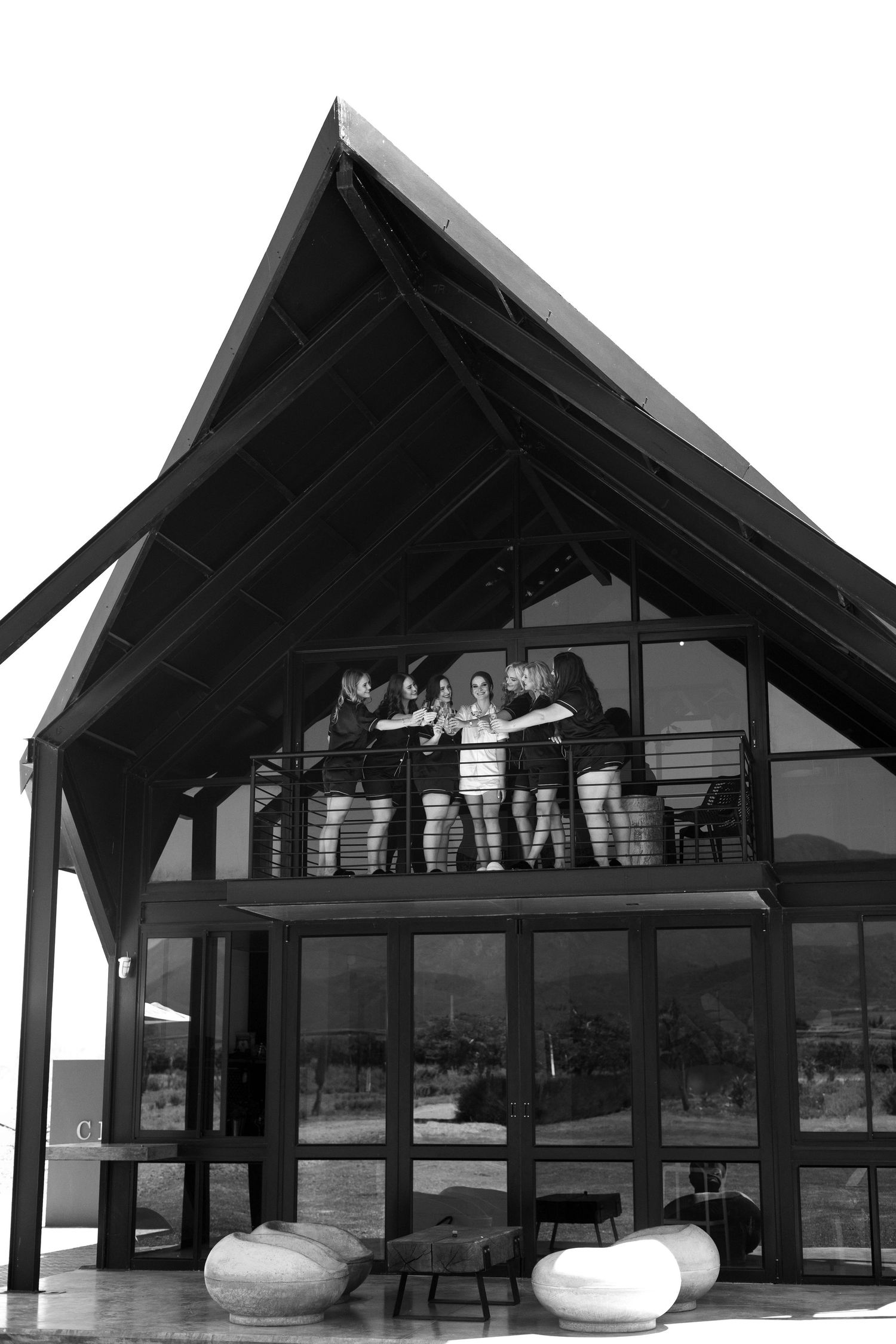 A modern architectural building with a peaked roof and outdoor space featuring modern white seating below the balcony area.