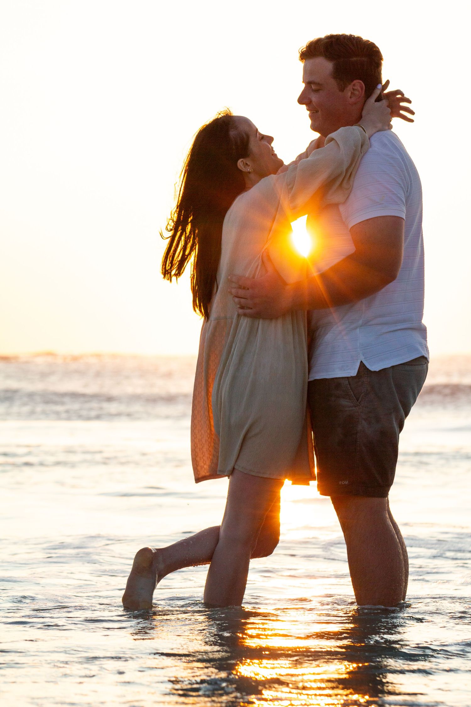 Romantic couple embracing in ocean water during golden sunset.