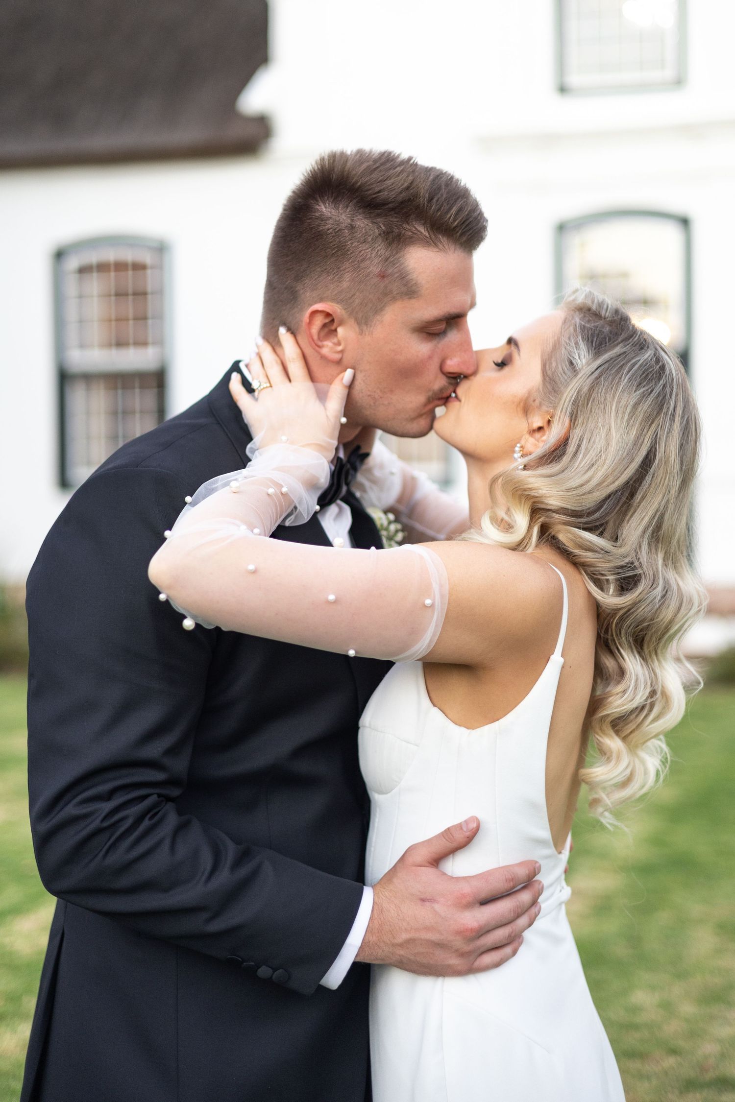 Romantic wedding kiss captured in garden setting with elegant white dress and black suit.