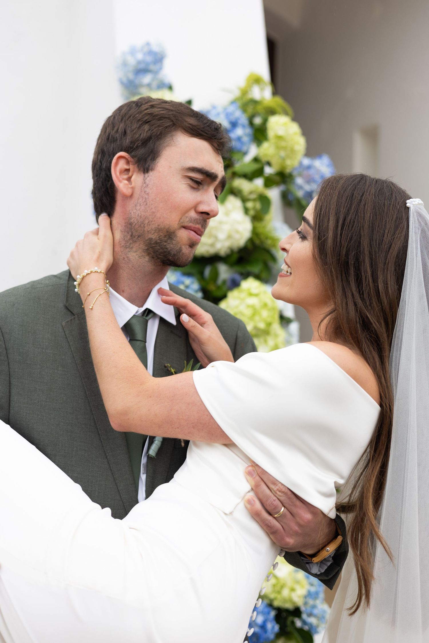 A romantic wedding couple shares tender kisses in a sequence of photos with white flowers and greenery in background.