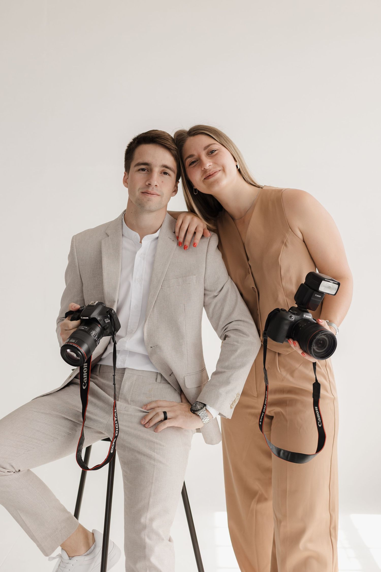 Photography duo in coordinated outfits pose with cameras against white background.