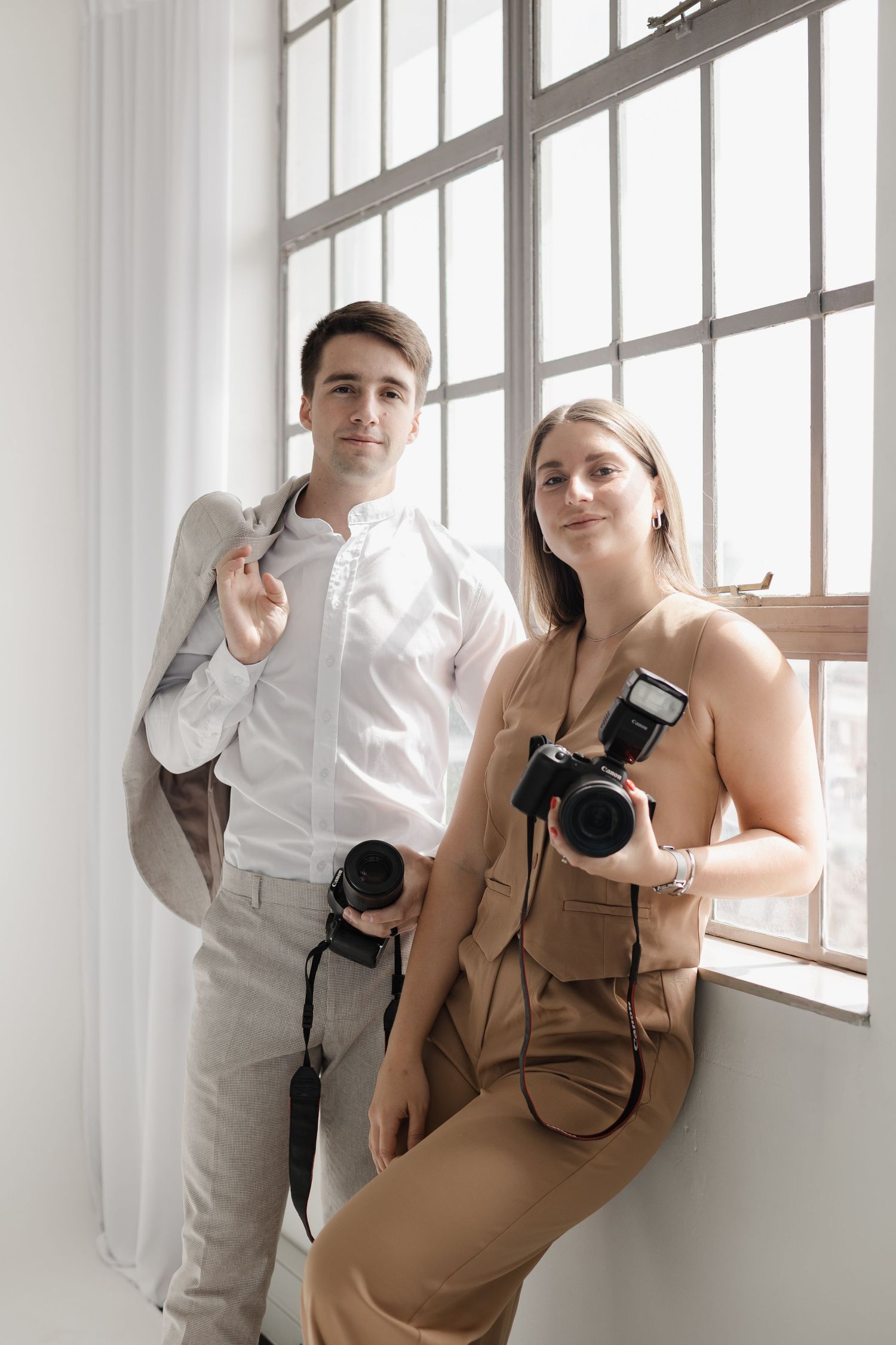 Professional photographers posing with cameras in a bright studio setting beside large windows.