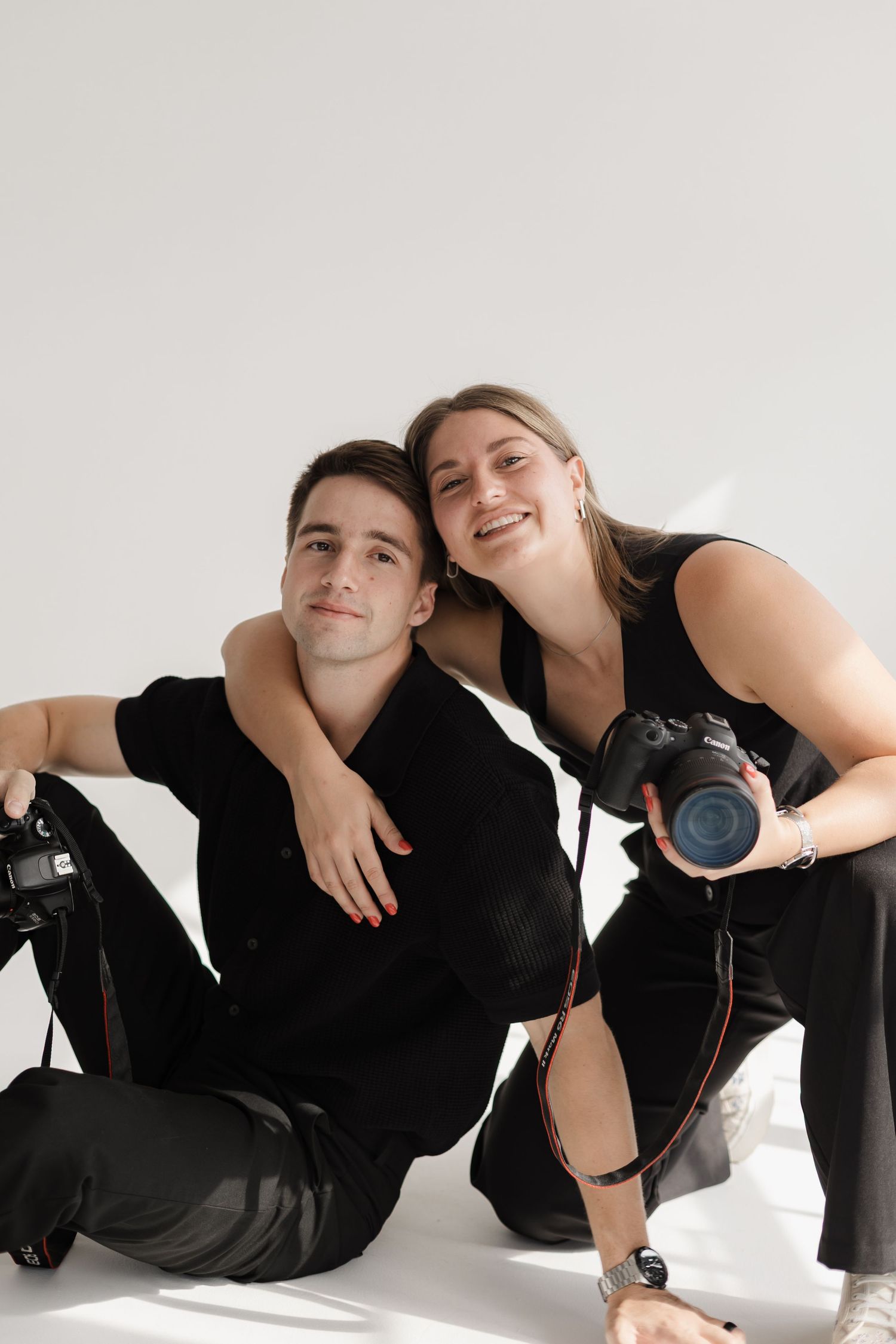 Photography team sits casually with cameras in minimalist studio setting.