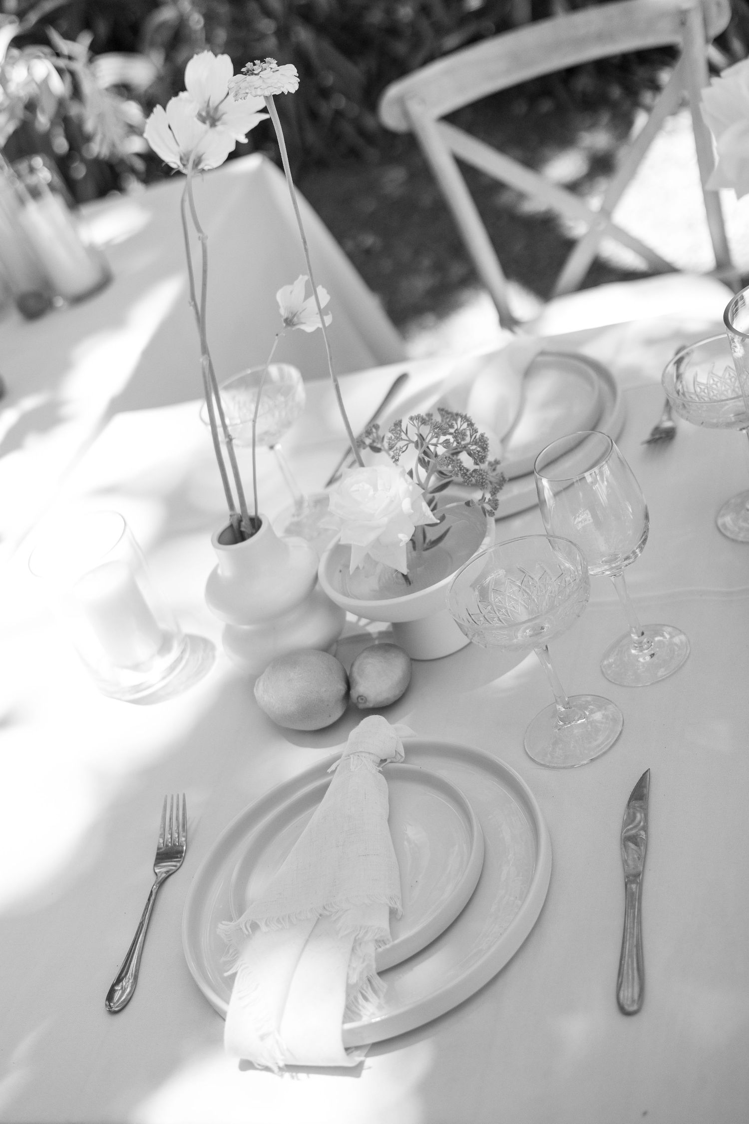 A monochromatic table setting with white linens, elegant dinnerware, wine glasses, and delicate flowers in a vase.