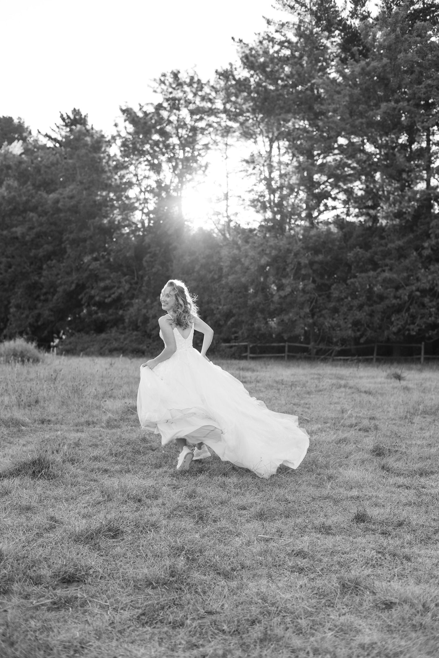 Black and white photo of bride twirling in her dress in an open field at sunset.