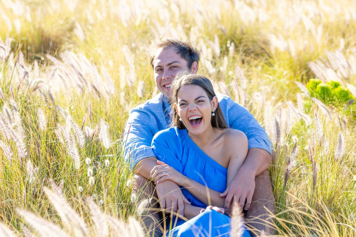 A couple laughing together in a sunlit field of tall grass.