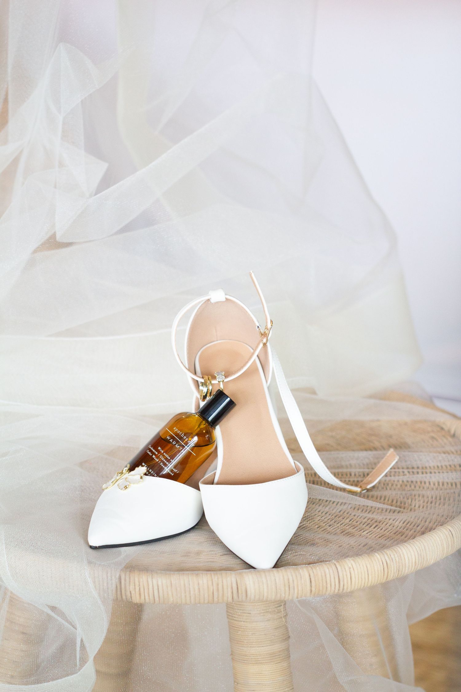 Elegant white bridal shoes and veil arranged on a woven surface with soft, dreamy lighting.