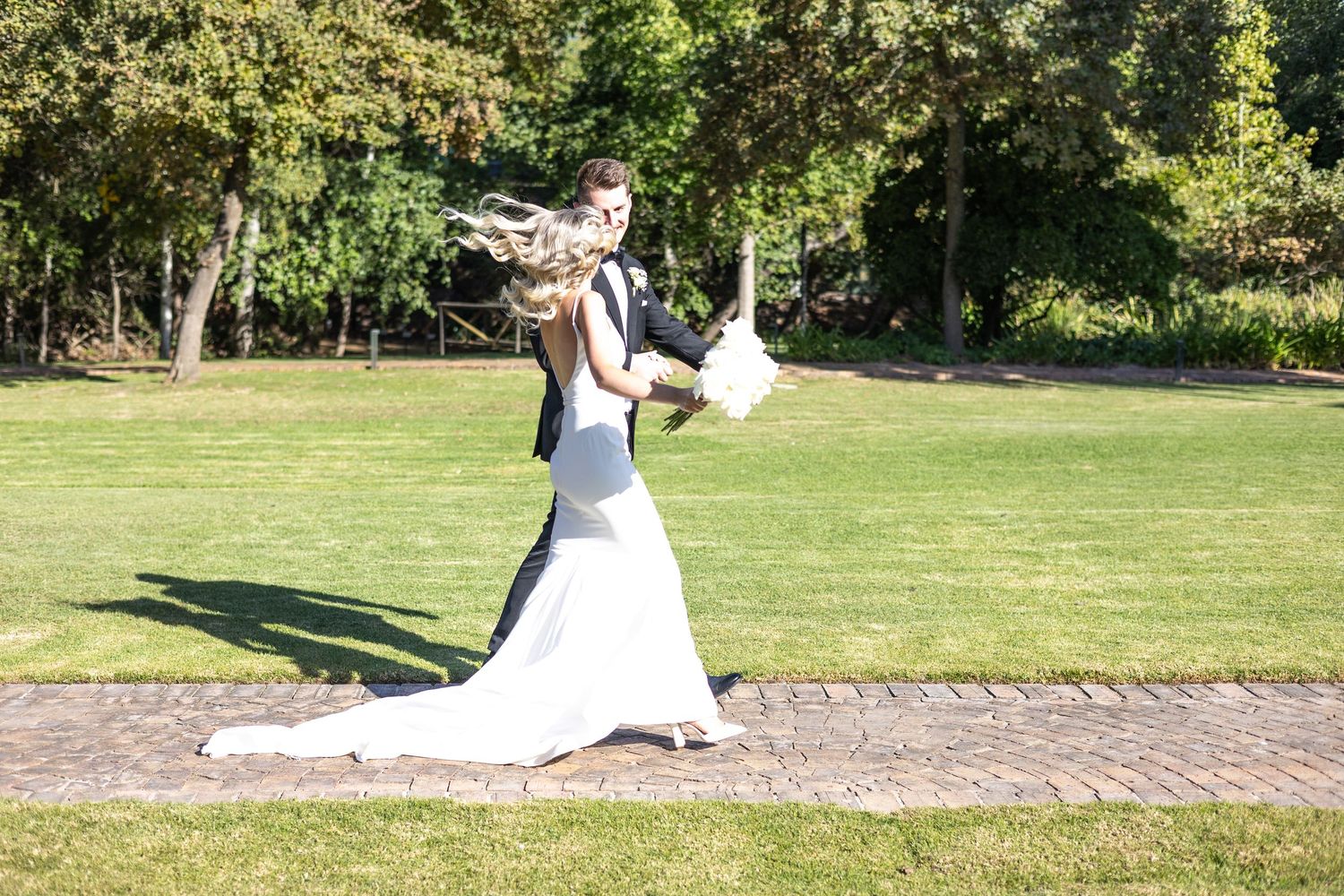 Wedding couple dancing and spinning joyfully on garden path during celebration.
