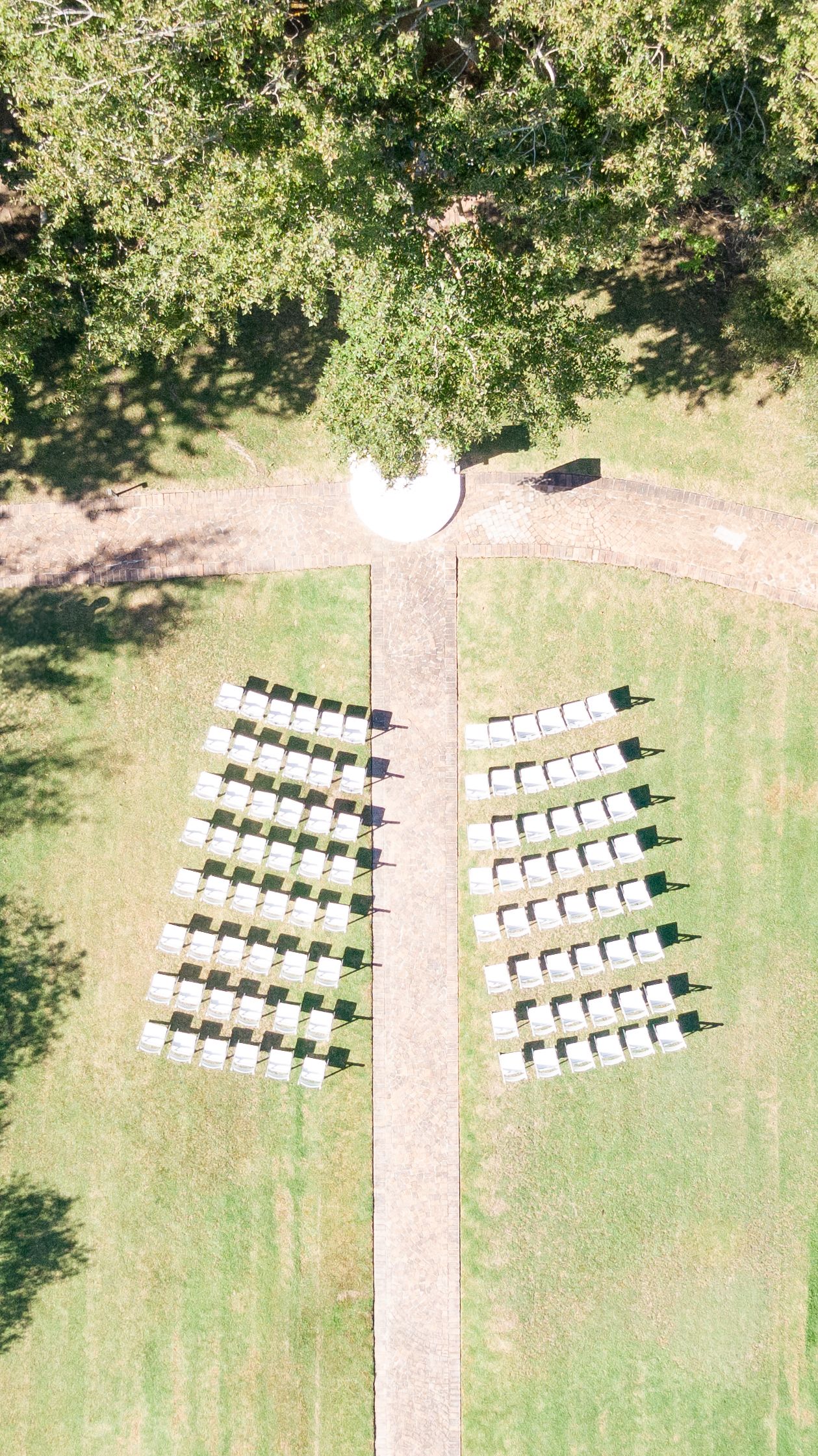 Aerial view of white wedding ceremony chairs arranged symmetrically on a grass lawn under trees.