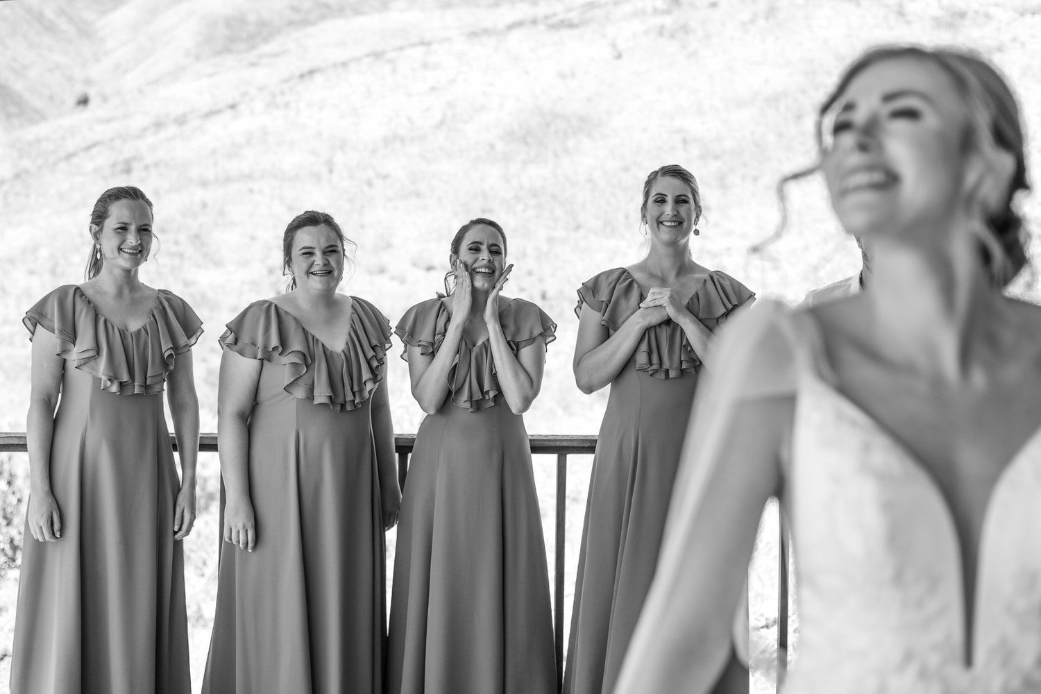 Black and white wedding scene showing bridesmaids in matching gray dresses standing behind smiling bride.
