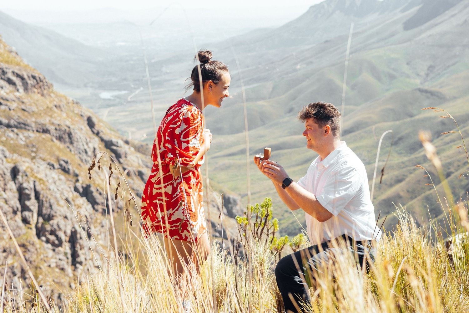 A marriage proposal taking place on a scenic mountain overlook with vast valley views.