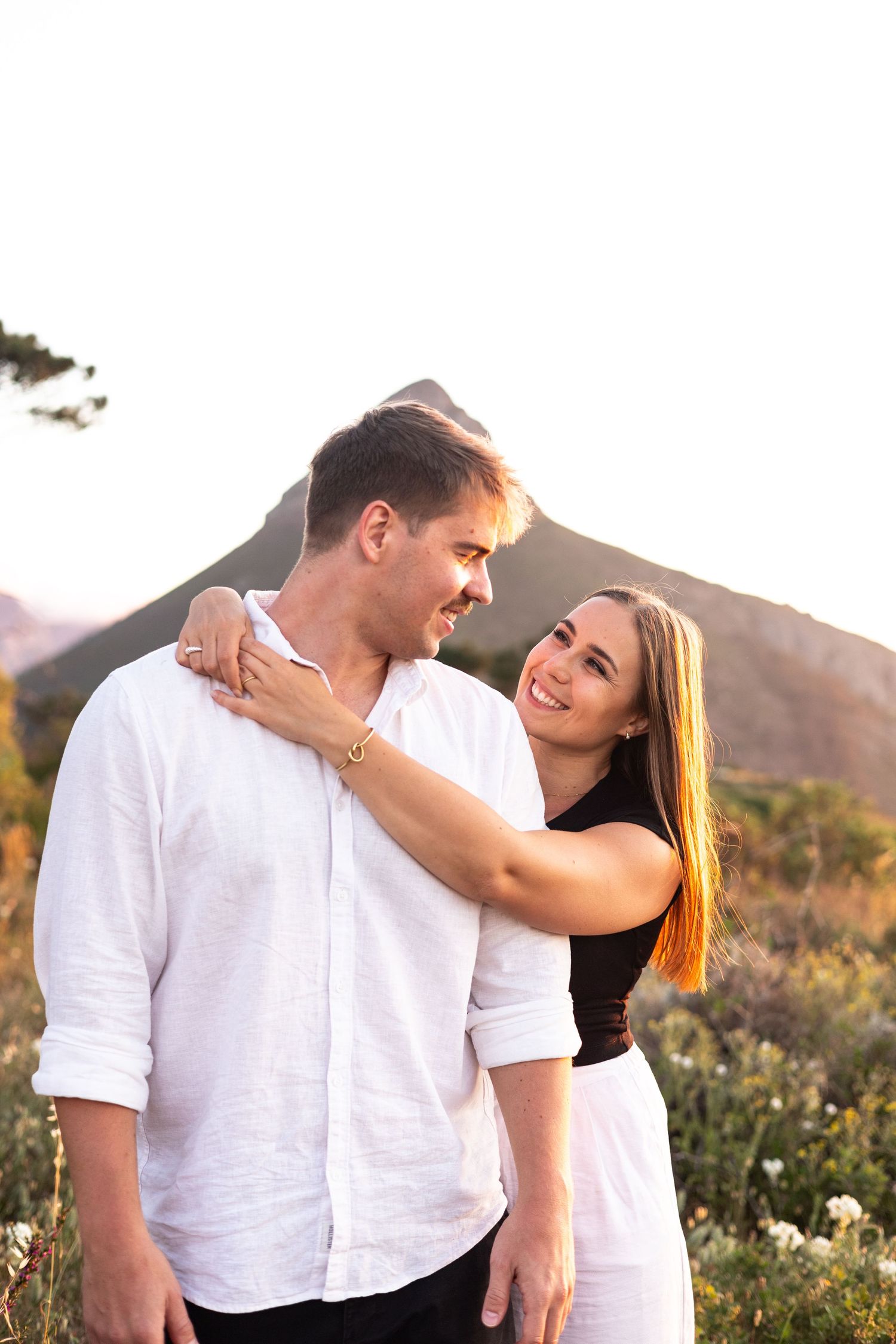 A couple shares an intimate moment at sunset with mountains in the background.