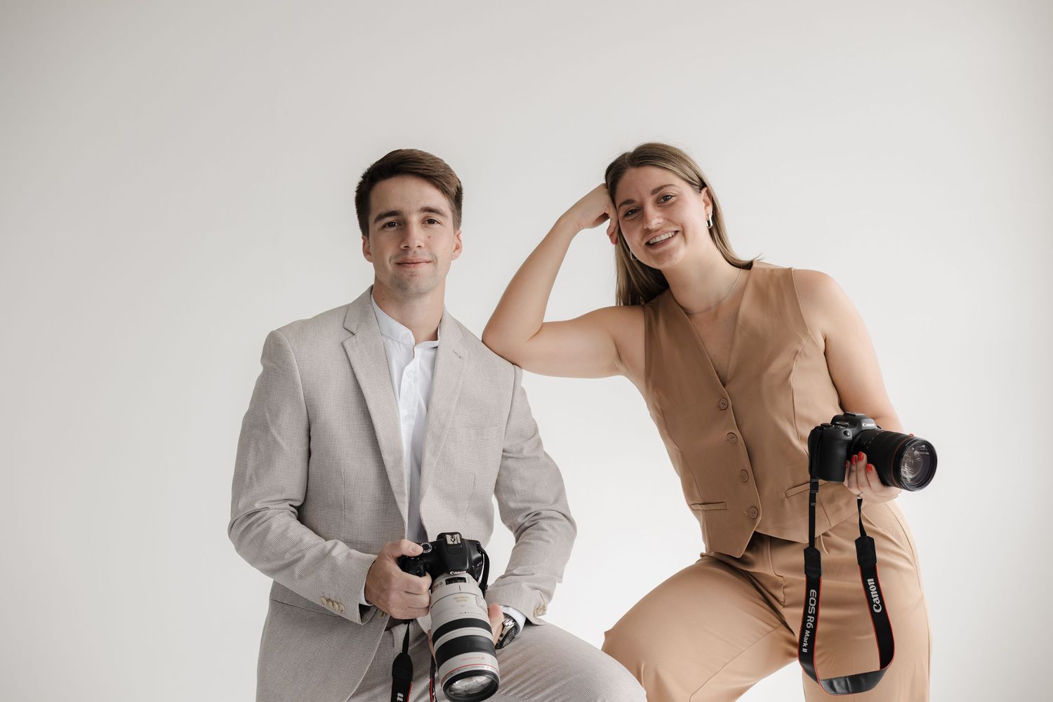 Two photographers with professional cameras posing against white studio background.