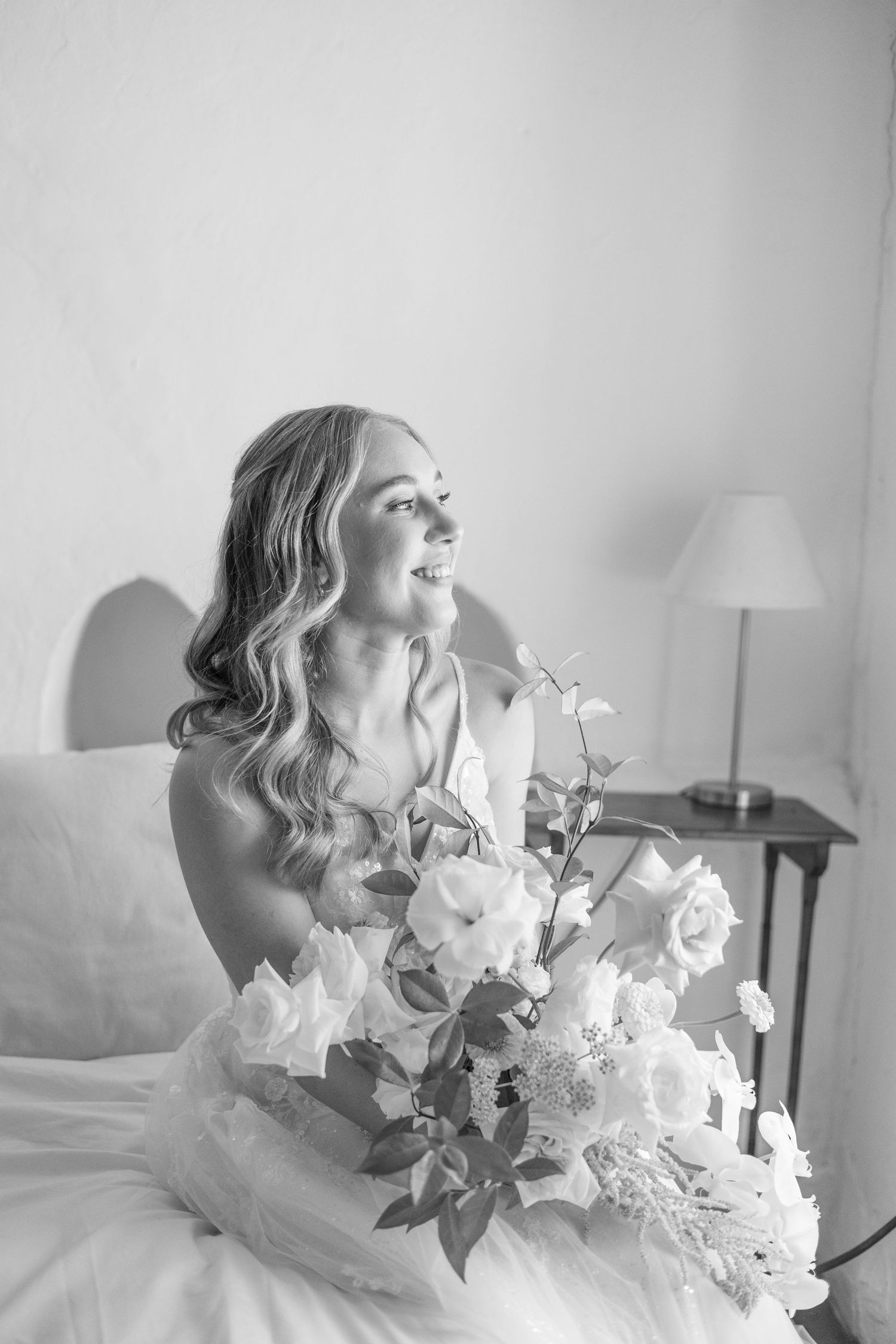 Black and white bridal portrait showing someone in a wedding dress sitting with a beautiful bouquet of white roses and flowers.