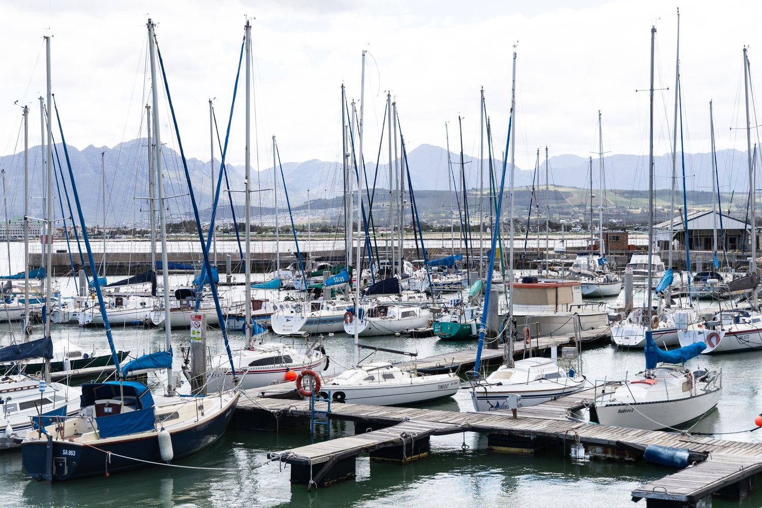Marina filled with sailboats and yachts against mountain backdrop.