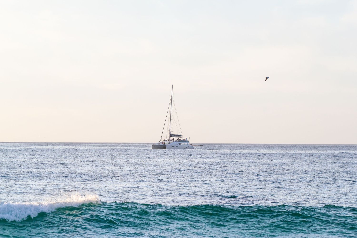 Sailboat floats on blue ocean waters against pastel sky.