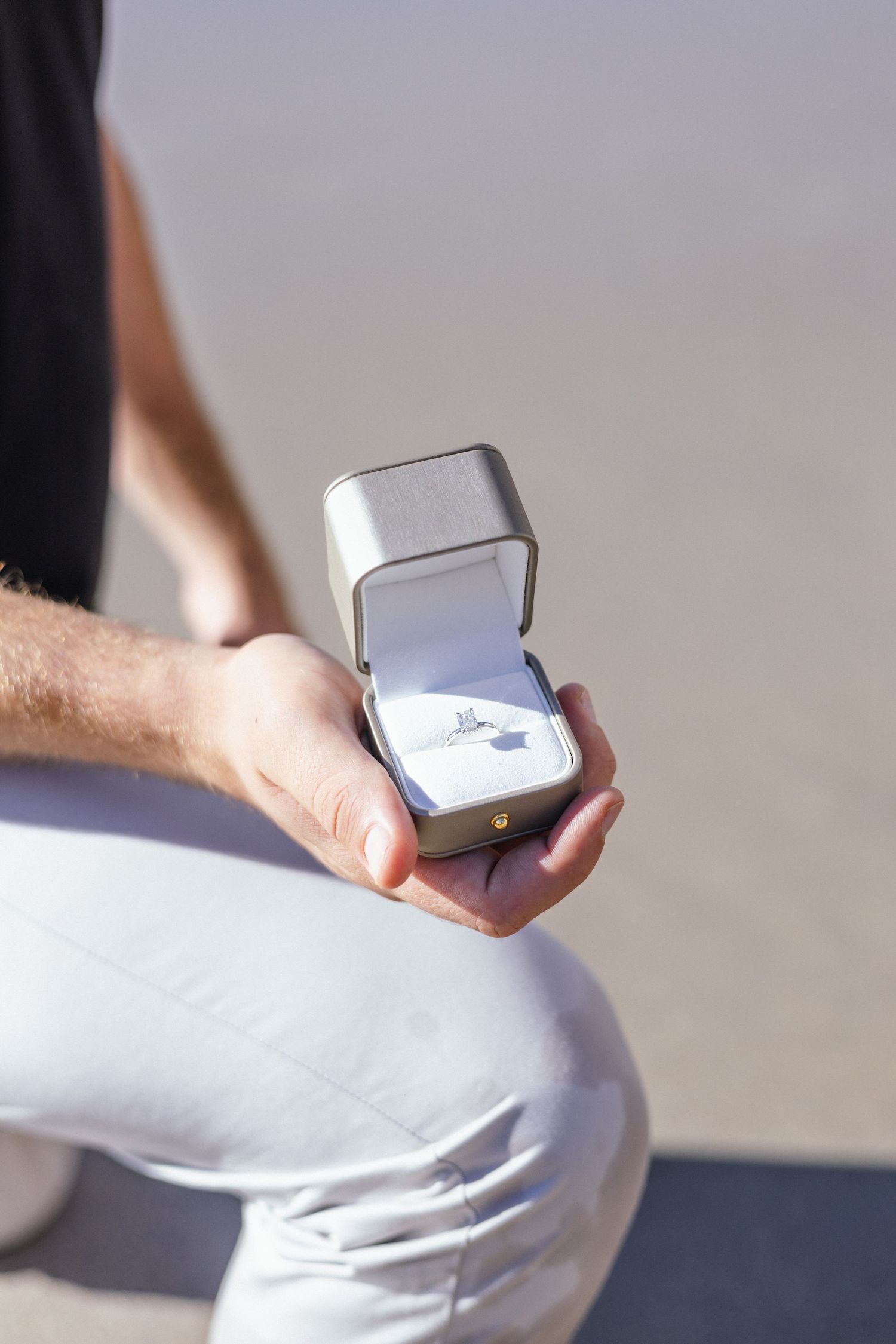 Close-up of engagement ring box being held on sunny beach.