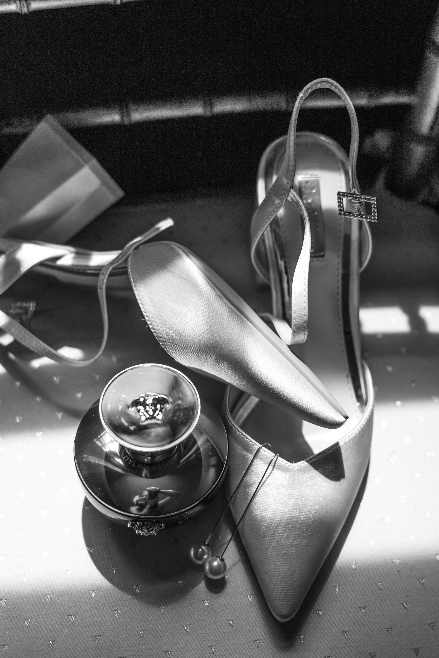 Black and white photo of elegant high heel shoe next to perfume bottle in dramatic lighting.