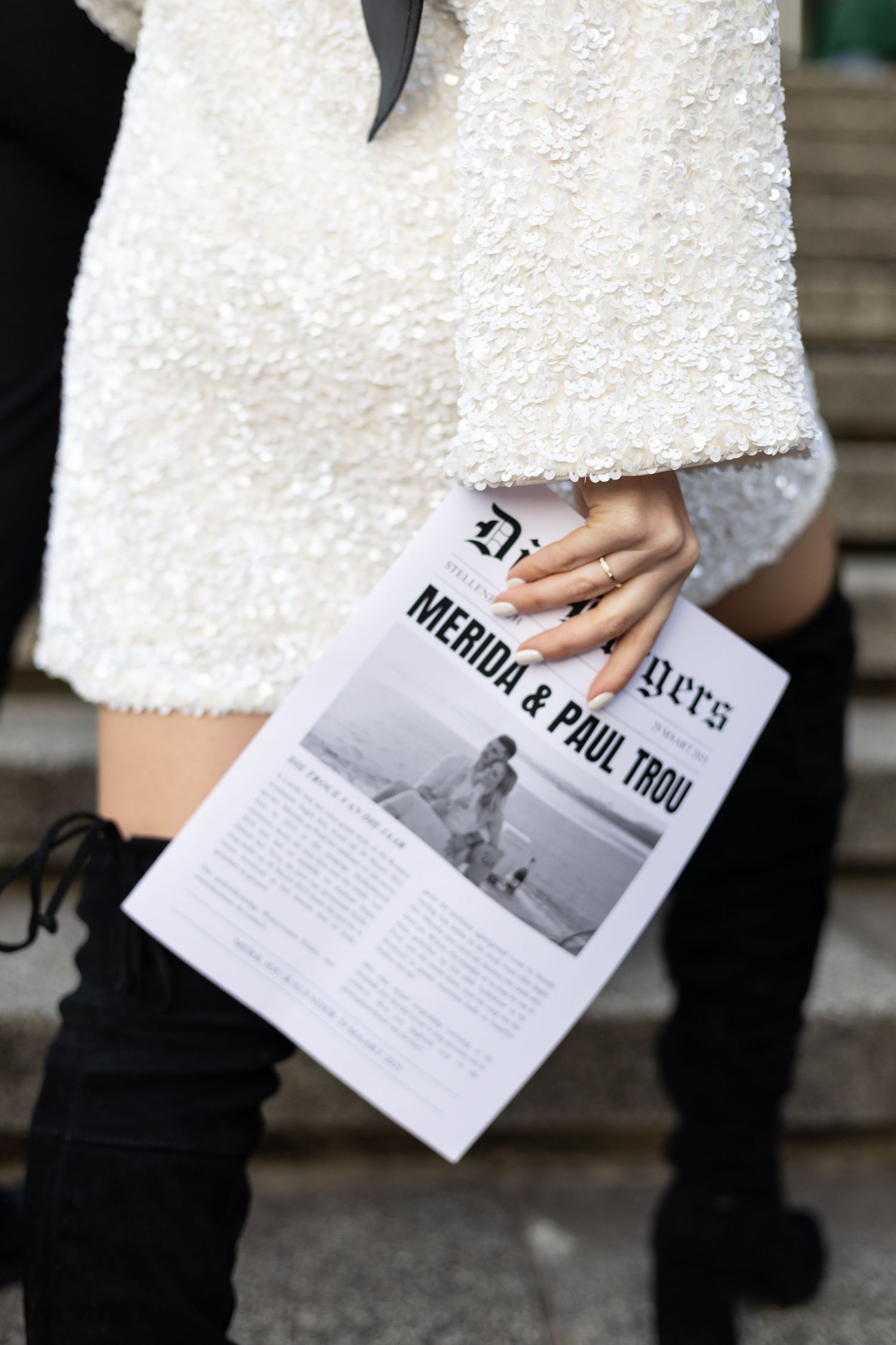 Close-up of hands holding a wedding program with black boots visible in the frame.