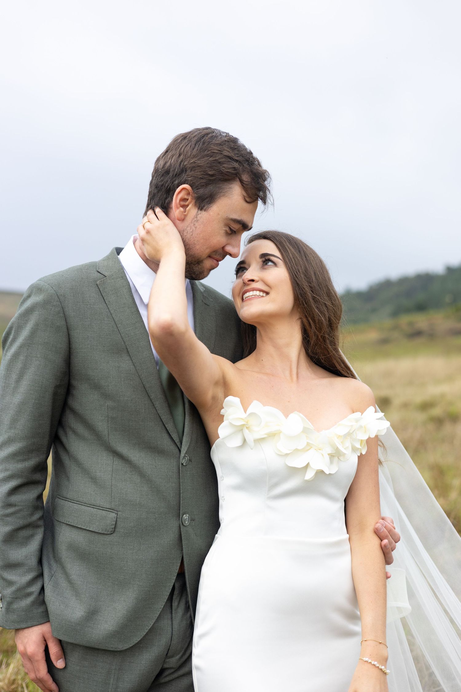 Close-up shots of newlyweds embracing in an outdoor setting with soft natural lighting and rolling landscape.