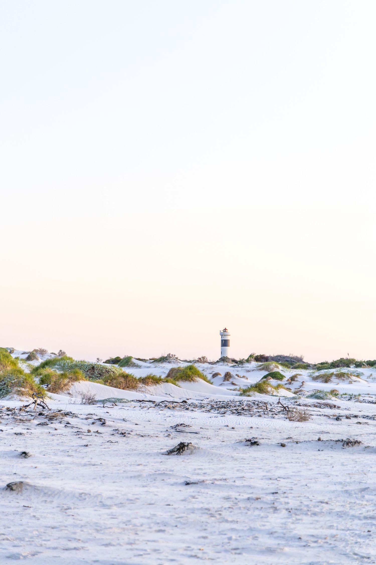Lighthouse visible in distance among sandy dunes during sunset.