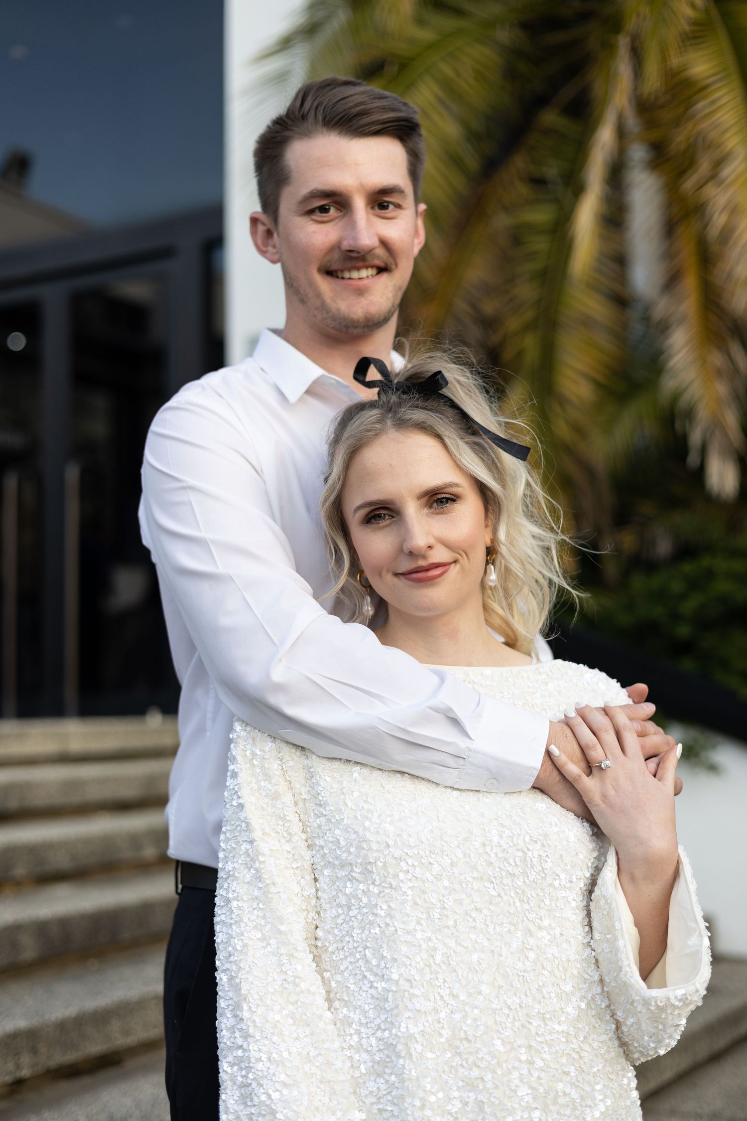 Formal couple portrait on white steps with palm trees in background.