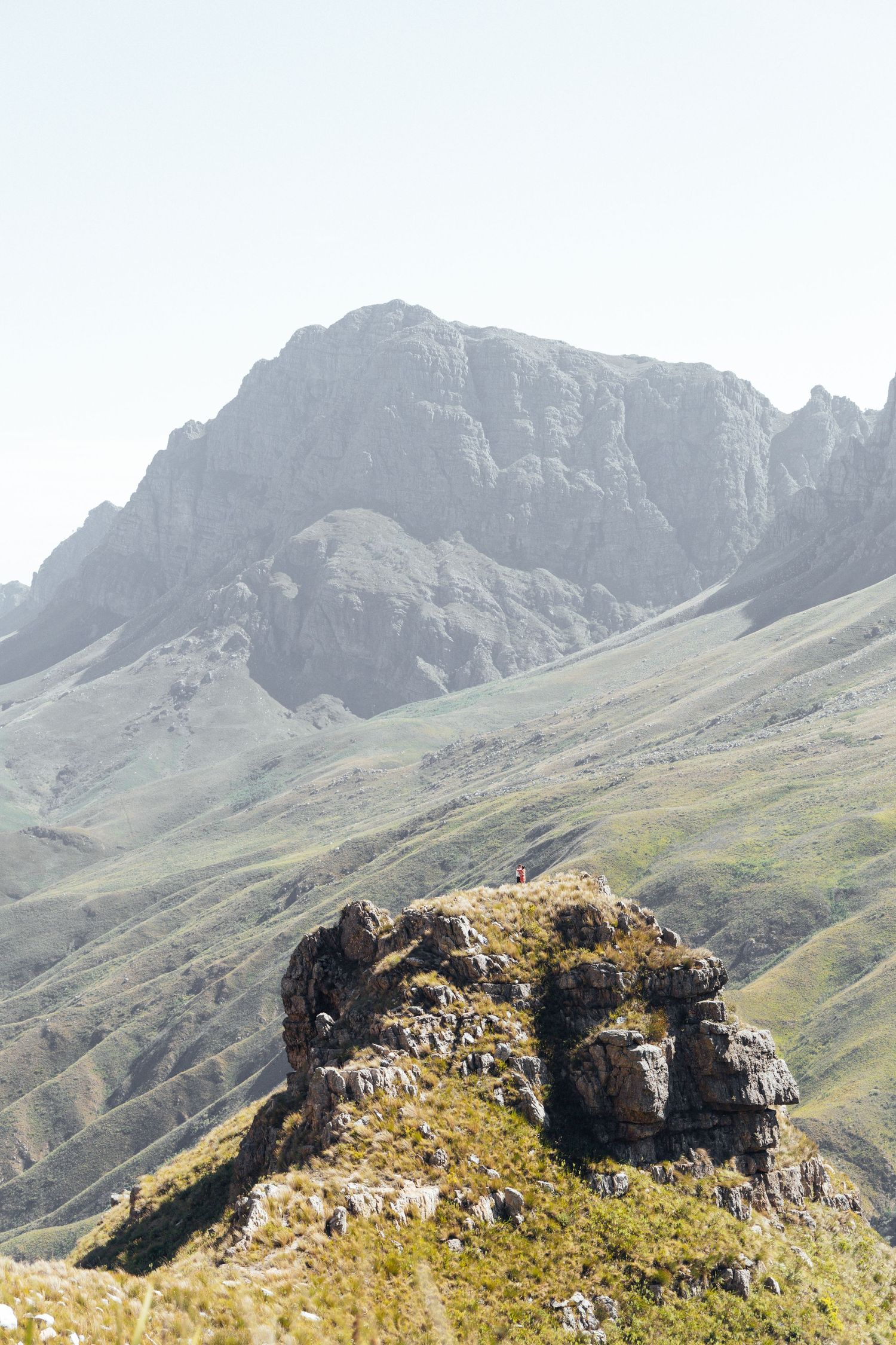 Dramatic mountain landscape with rugged peaks and a rocky outcrop in the foreground against a misty sky.