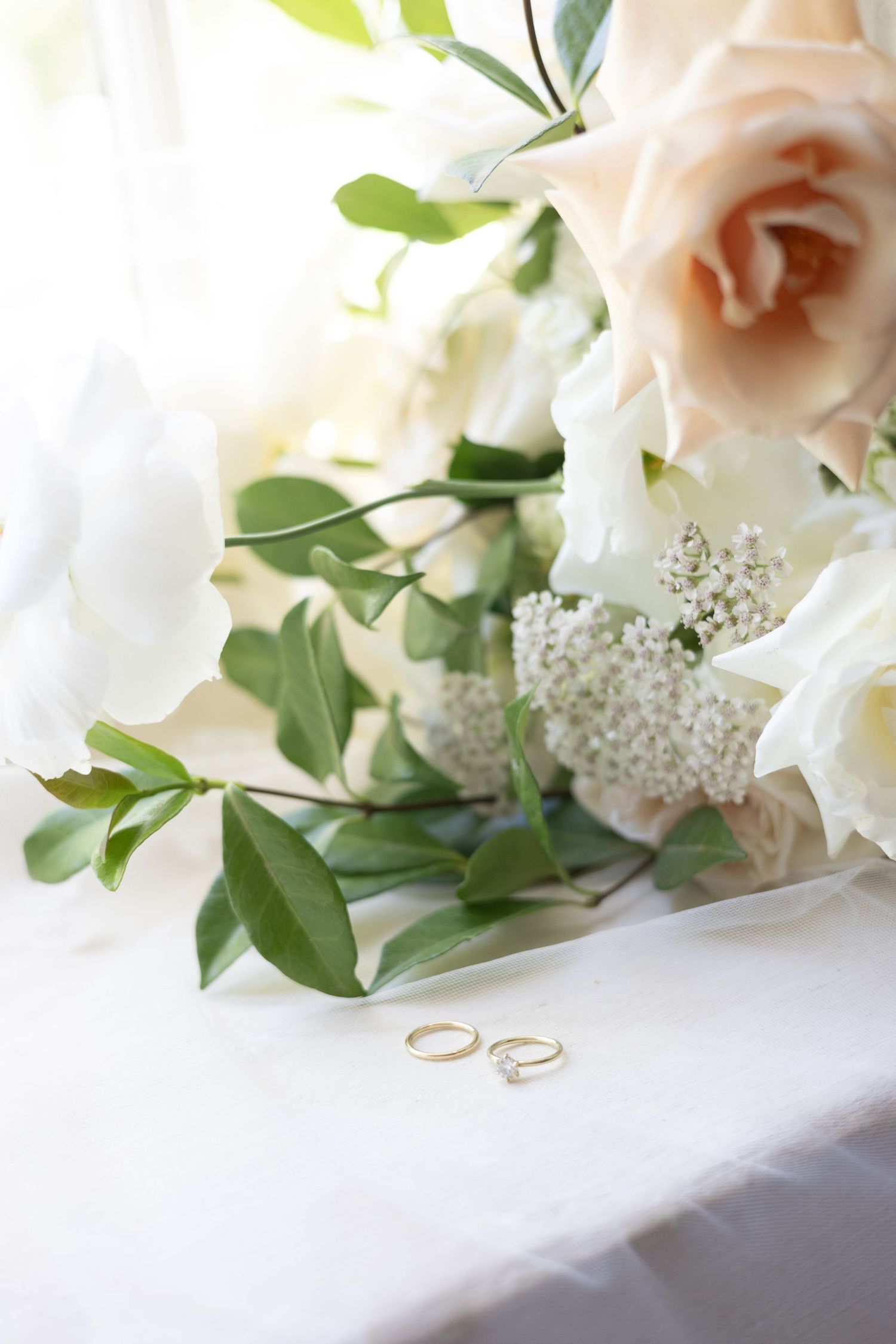 Romantic wedding still life with pink and white roses, greenery and gold wedding bands.
