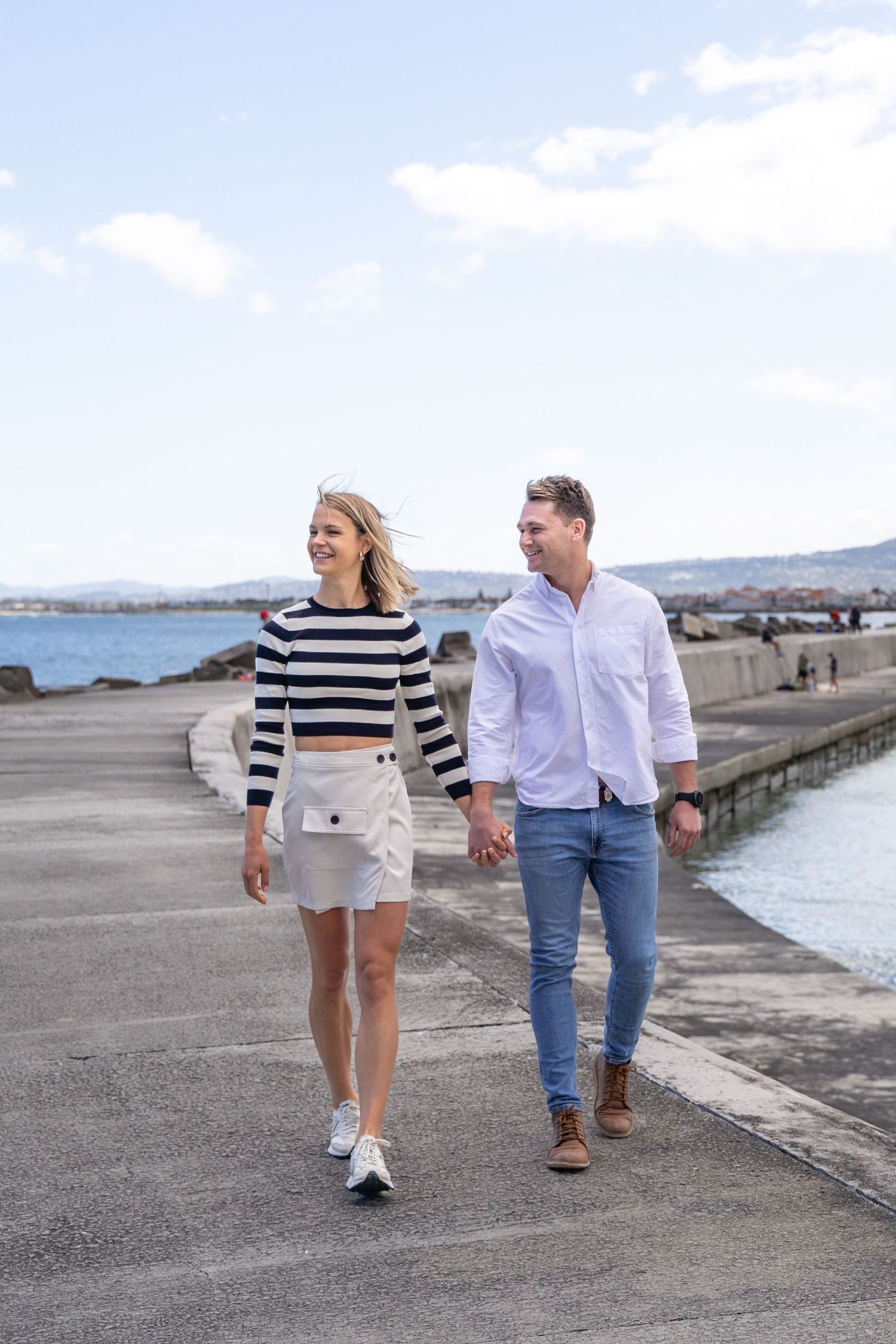 Couple walking together on coastal pier in casual attire.