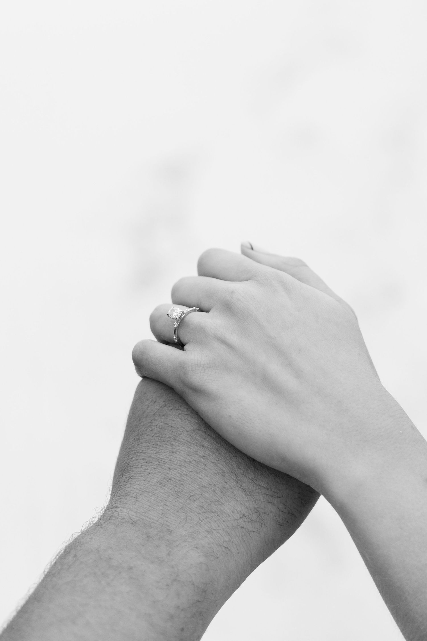 Black and white close-up of two hands clasped together with engagement ring visible.