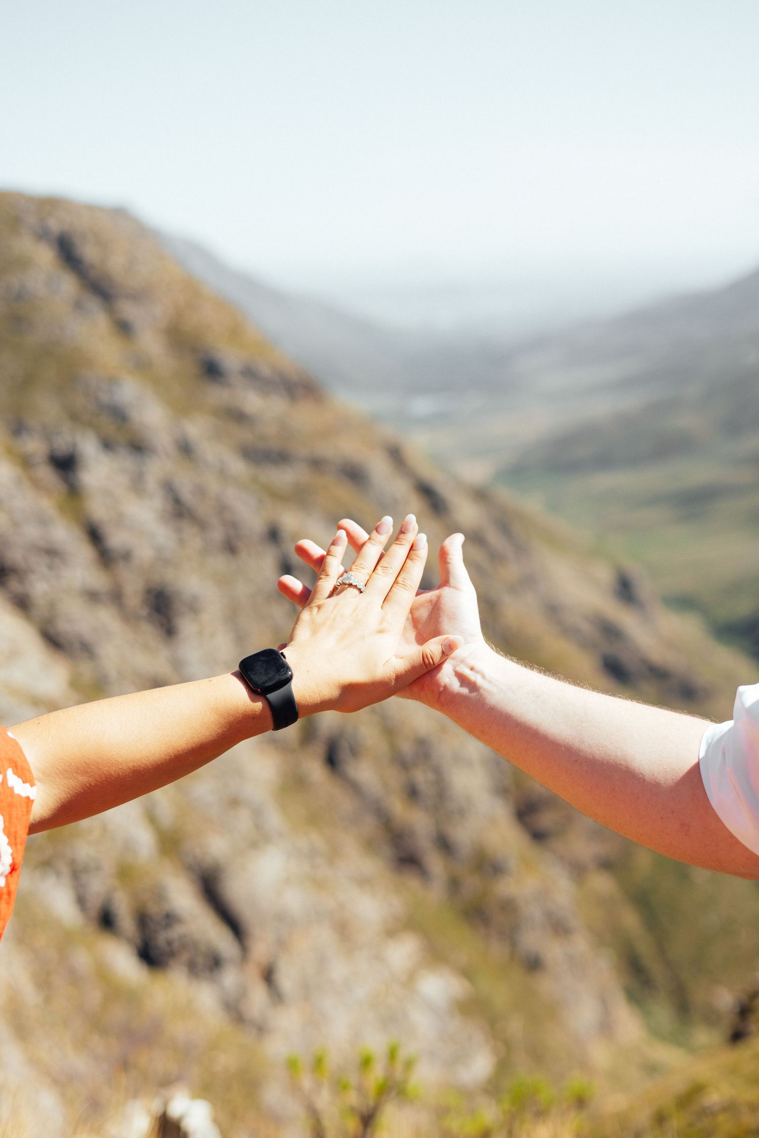 Two hands reach out to high-five against a scenic mountain valley backdrop.