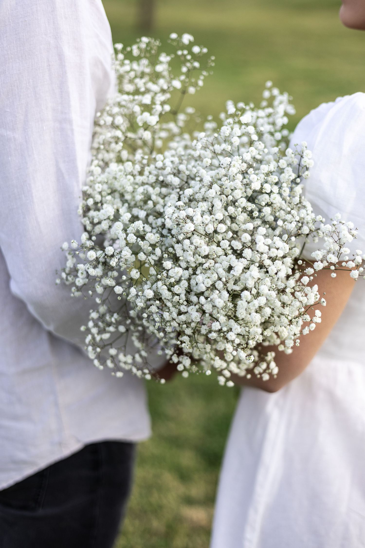 Close-up of delicate baby's breath bouquet held against white clothing.