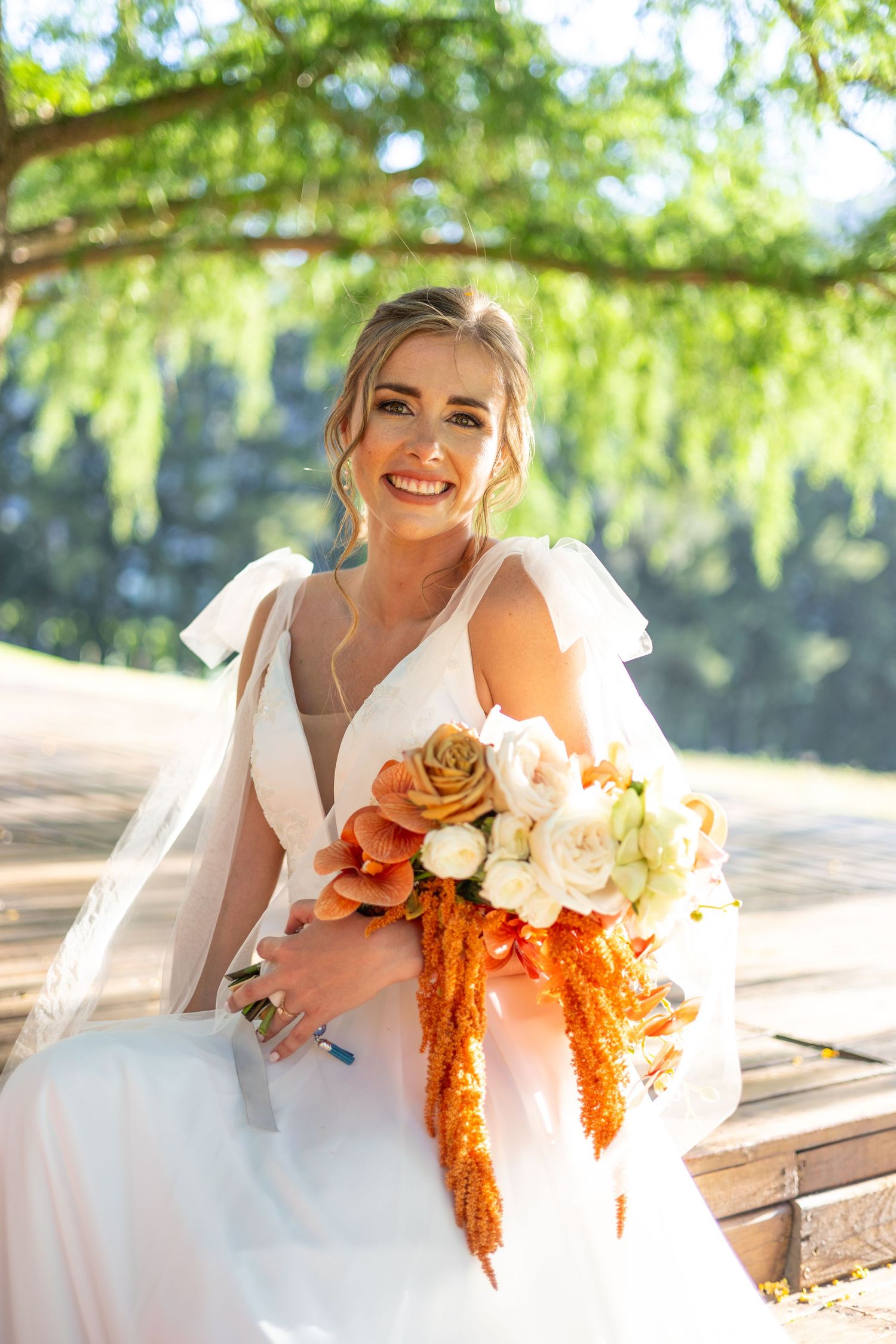 A bride in a flowing white dress holds a vibrant bouquet of orange and white flowers with cascading amaranth.