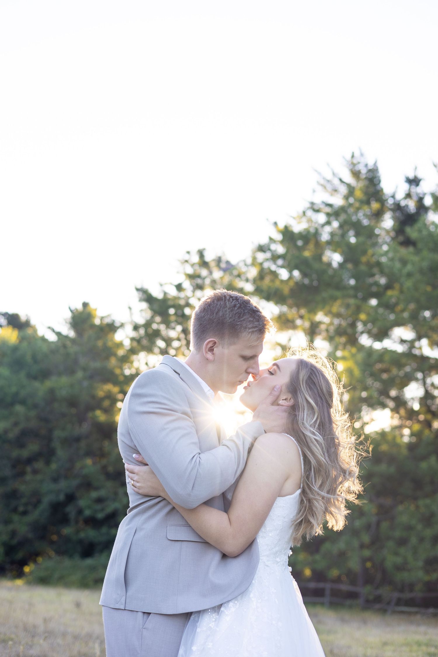 Romantic sunset portrait of newlyweds embracing in an outdoor setting with golden backlighting.