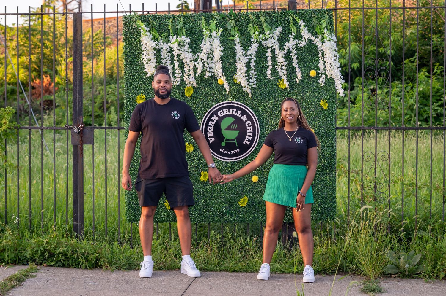Two people standing in front of decorative garden wall with floral accents.