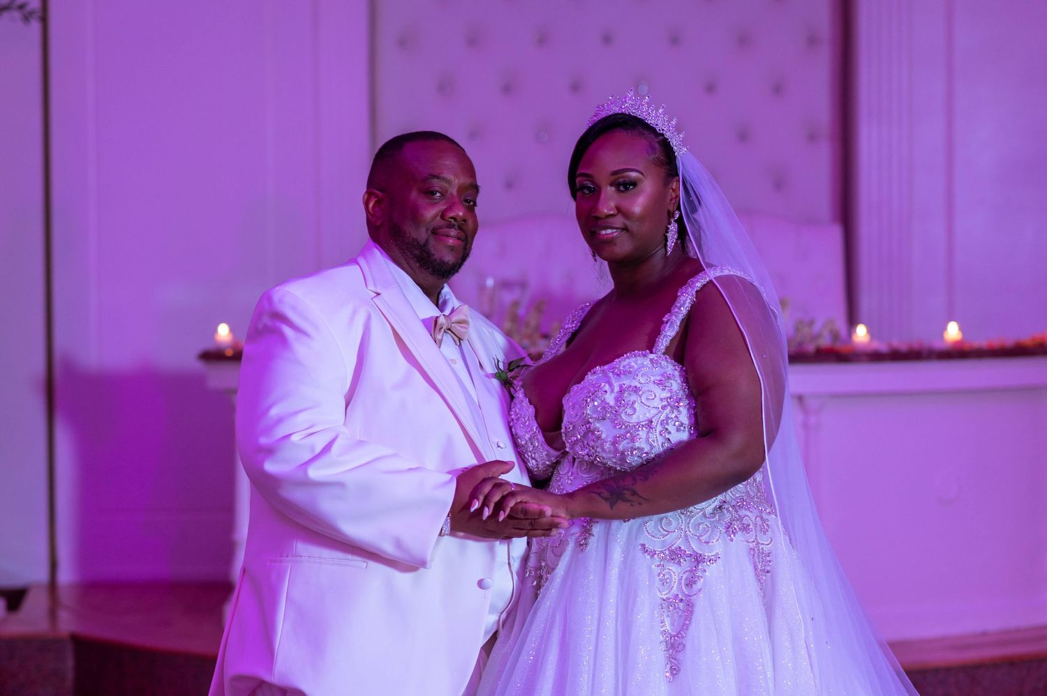 Wedding couple in white attire dancing together under purple lighting at their reception celebration.