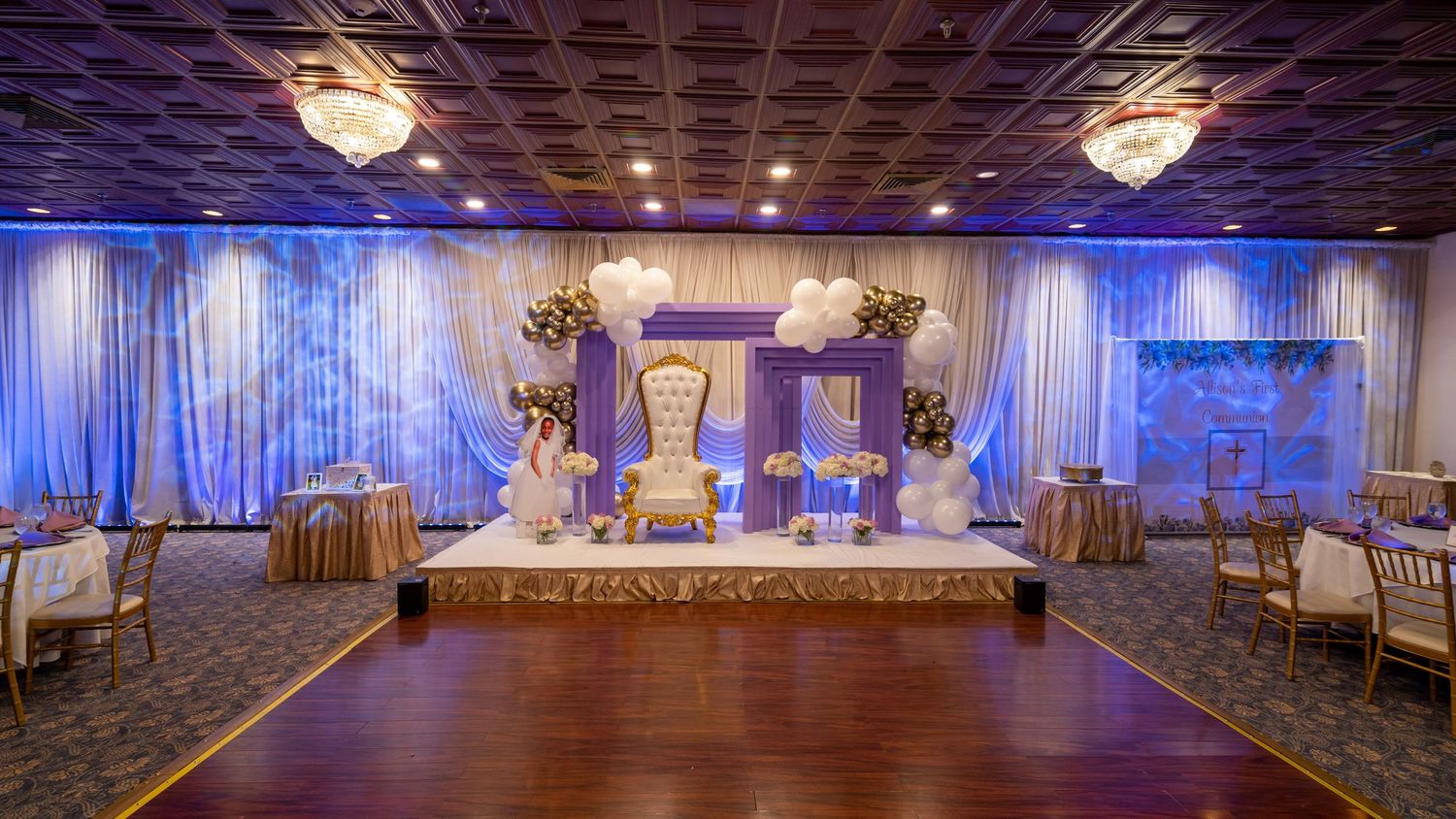 Elegant wedding venue setup with blue lighting, white draping, and golden throne chairs on stage.