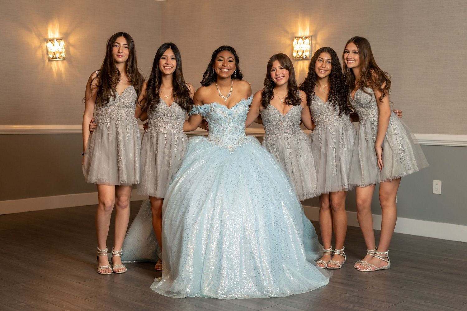 Bridal party poses in light blue ballgown and silver bridesmaid dresses in elegant venue.