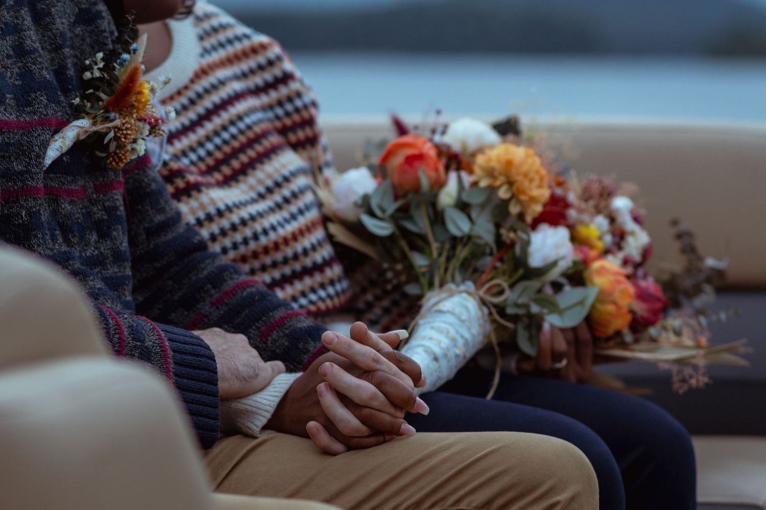 A cozy beach engagement scene with autumn flowers and intertwined hands at sunset.