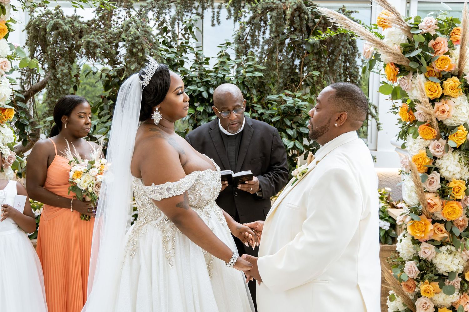 Outdoor wedding ceremony under floral arch with orange and white blooms.