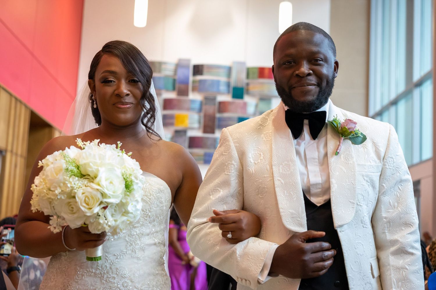 Wedding couple posing with white floral bouquet against colorful modern art wall.