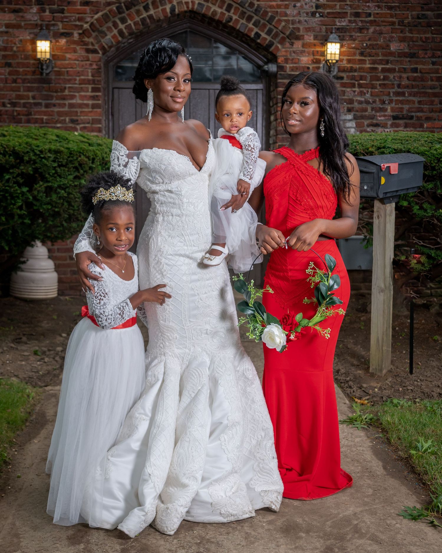 Wedding party poses together in front of brick wall with white and red dresses and formal attire for outdoor portraits.