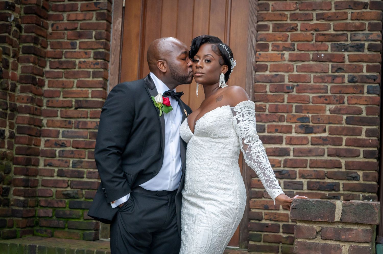 A bride and groom share a romantic moment against a rustic brick wall backdrop during their wedding celebration.
