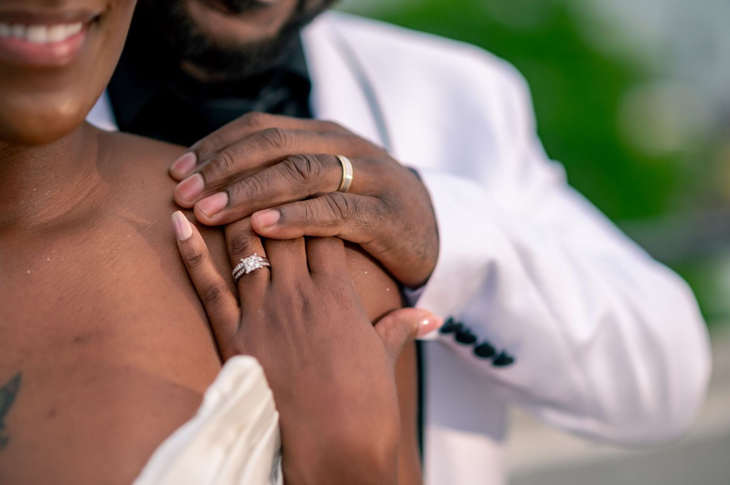 Close-up of a newlywed couple holding hands, showcasing wedding rings, bride in white dress, groom in white suit.